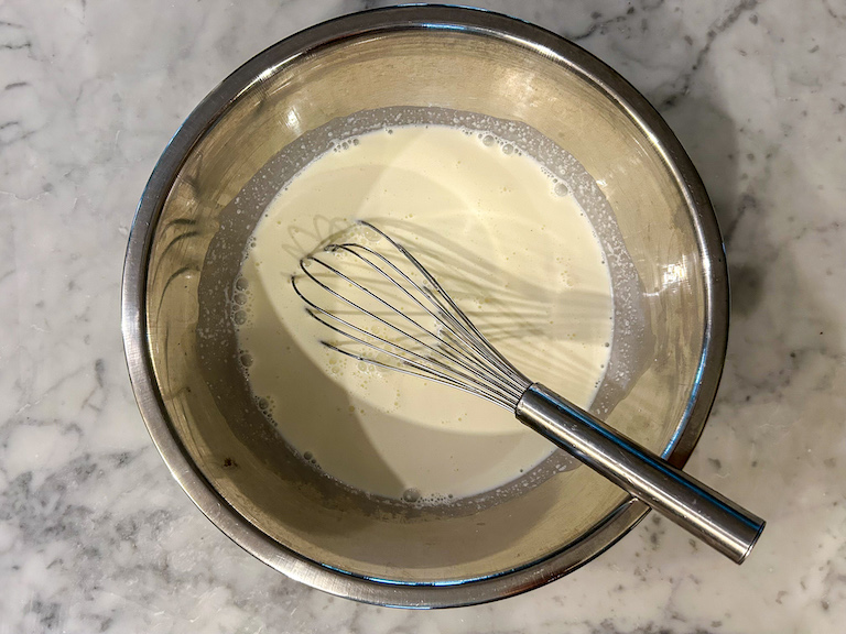 Cream, milk, and sugar in a metal bowl with a whisk