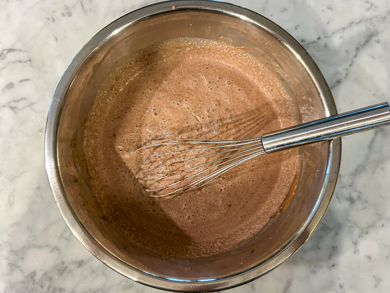 Chocolate ice cream base in a metal bowl with a whisk