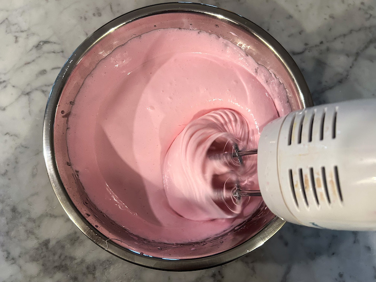 Pink marshmallow fluff in a bowl with a hand mixer
