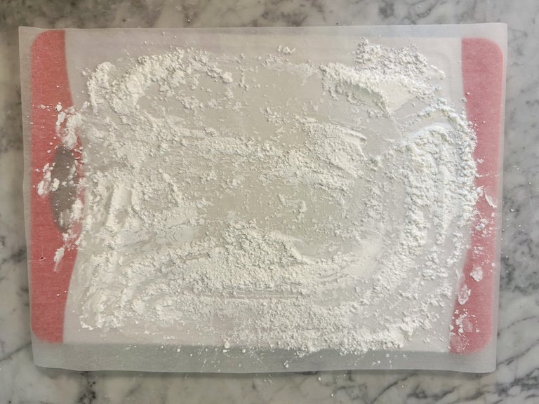 A sheet of parchment on a cutting board, dusted with powdered sugar and cornflour