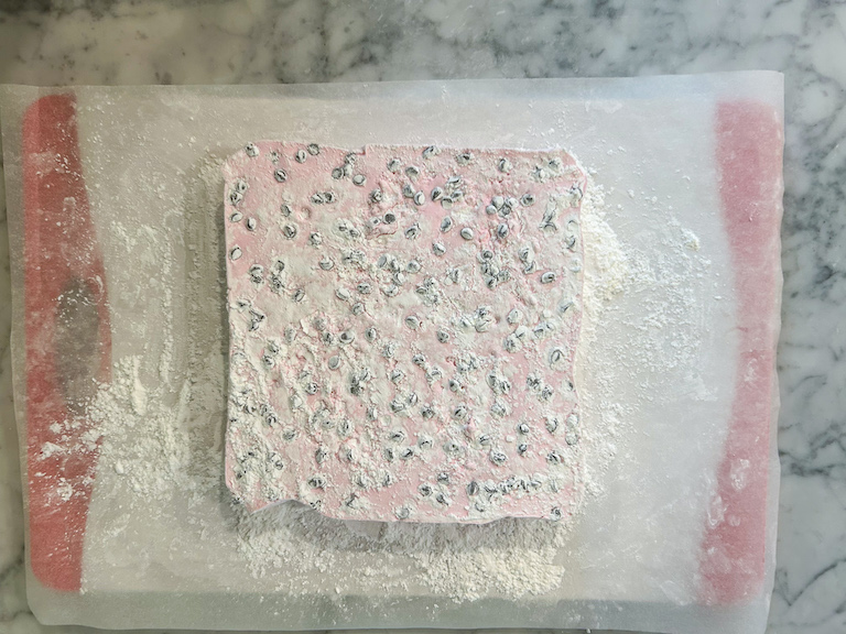Pink marshmallow slab on a sheet of parchment, coated in powdered sugar and cornflour