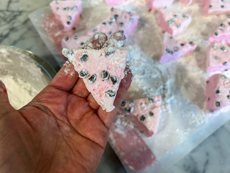 Hand holding a pink triangle shaped marshmallow with chocolate chips on top