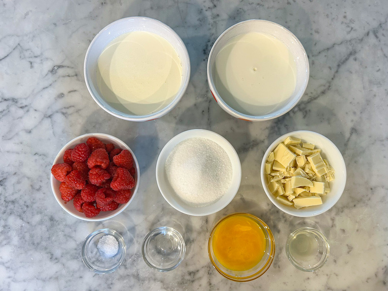 Ingredients for making raspberry white chocolate ice cream, arranged on a marble surface