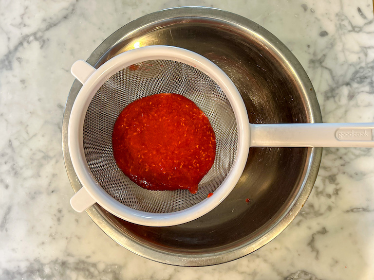 Passing pureed raspberries through a mesh strainer