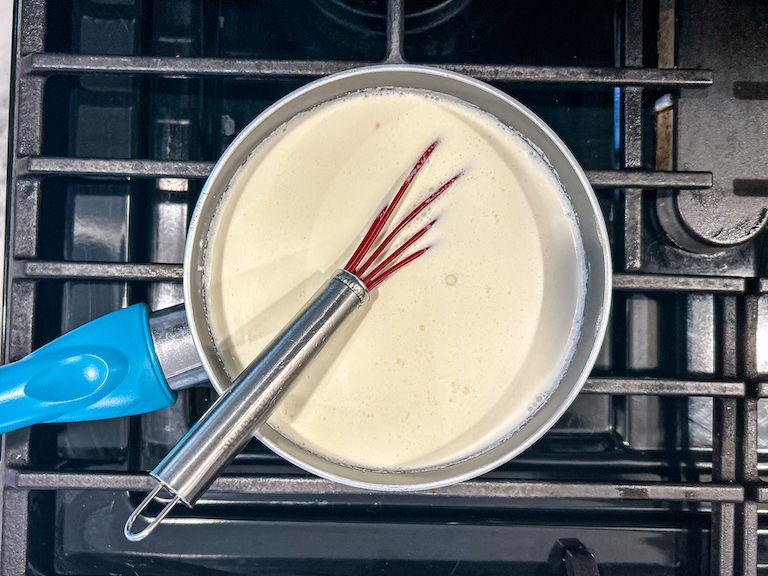 Ice cream base in a saucepan on the stovetop with a silicone whisk