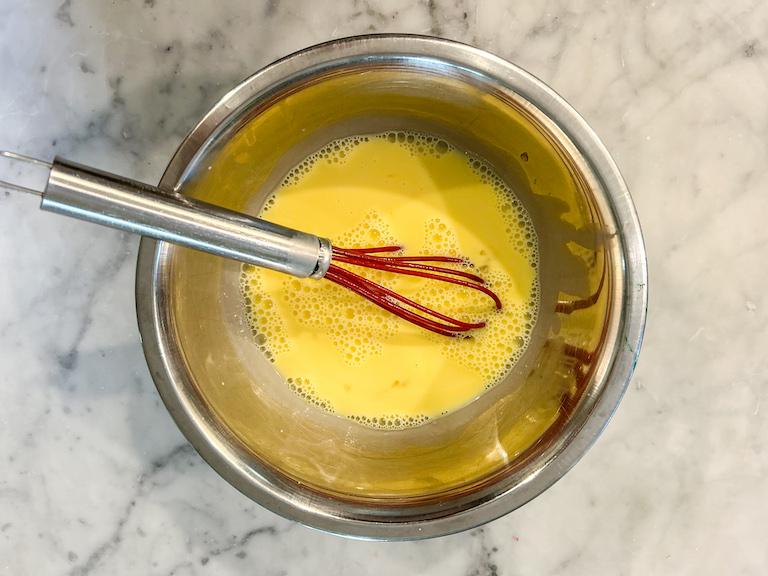 Whisking together eggs and cream in a metal bowl