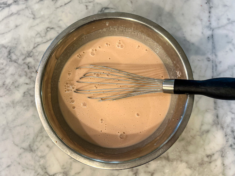 Raspberry ice cream base in a metal saucepan with a whisk