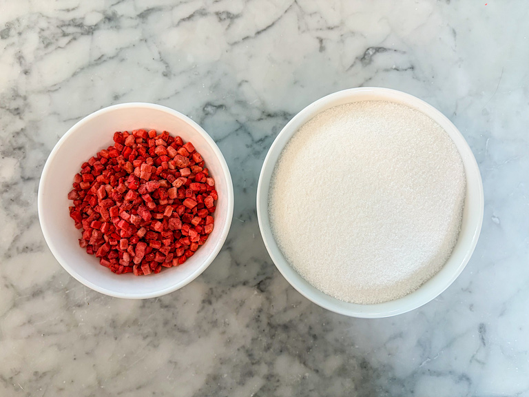 A dish of freeze dried strawberries and a dish of sugar on a marble surface