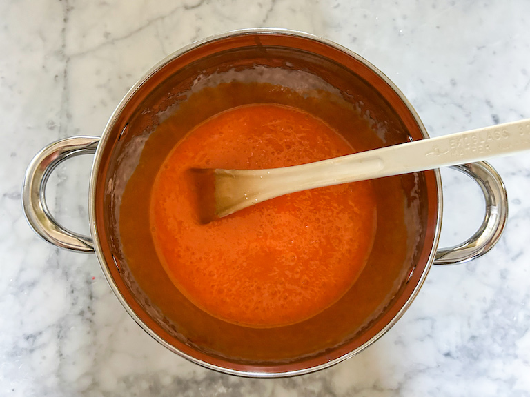 Melted orange marshmallow in a stock pot with a spoon