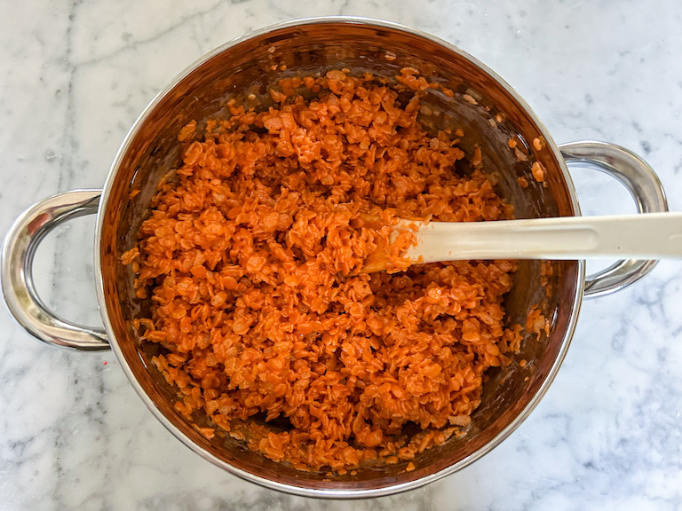 Orange rice krispie treat mixture in a stock pot with a spoon