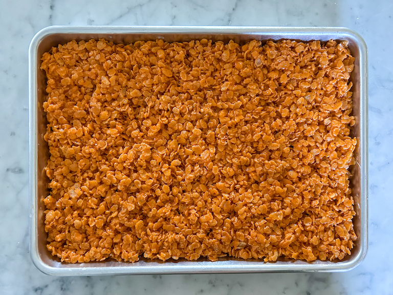 Orange krispie treat mixture pressed into a metal pan