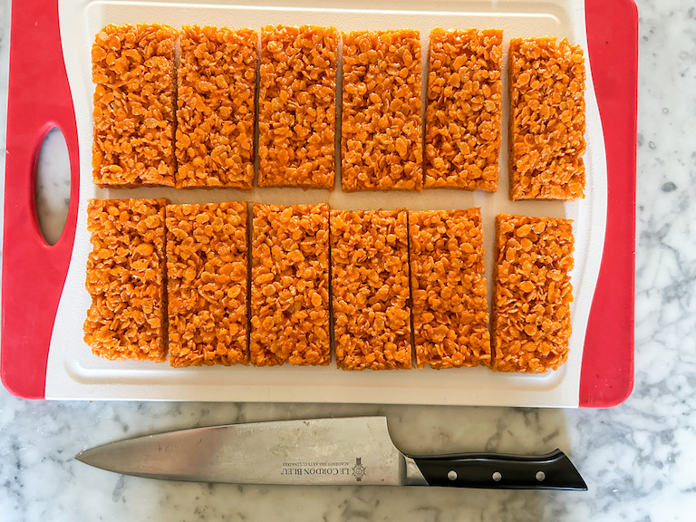 Krispie treat rectangles arranged on a cutting board with a chef's knife