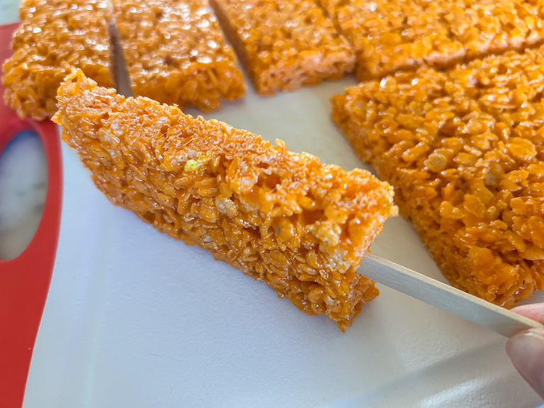Hand holding a popsicle shaped cereal treat against a white cutting board