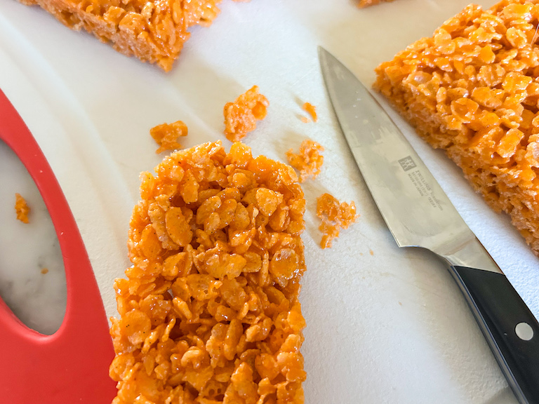 Paring knife trimming the edges of an orange cereal treat