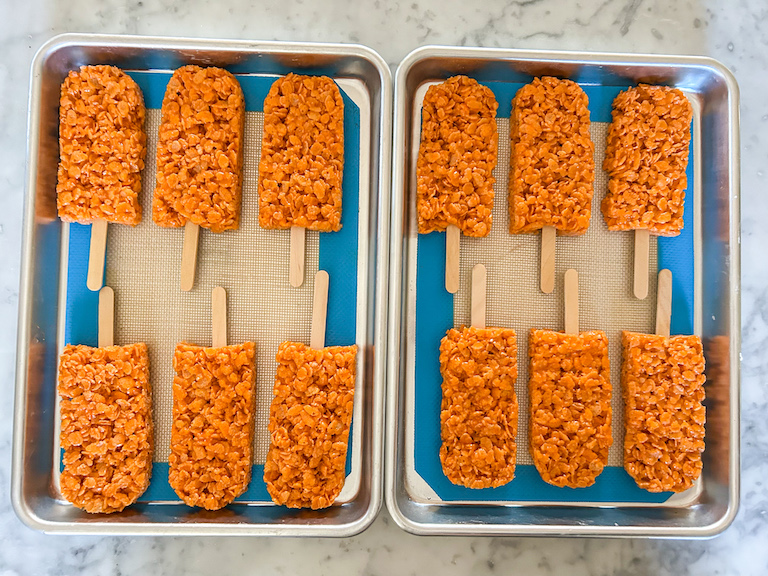 Orange krispie treat pops arranged on two small trays