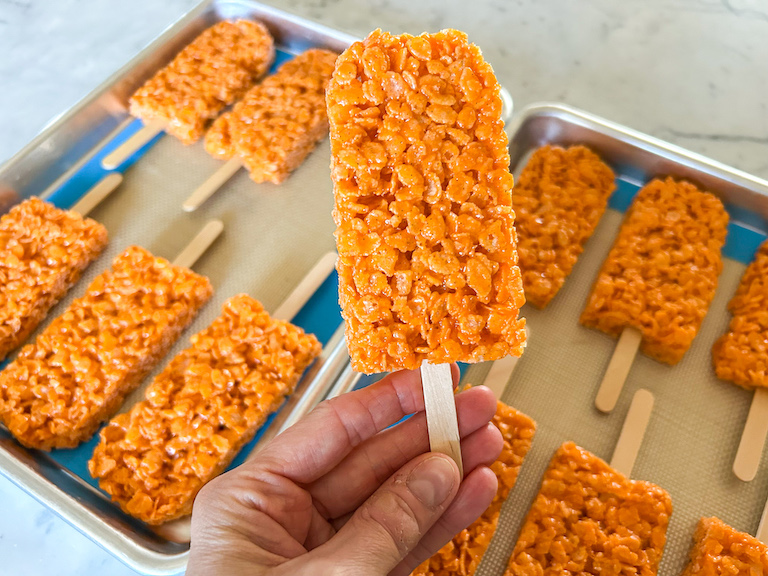 Hand holding an orange rice krispie treat popsicle