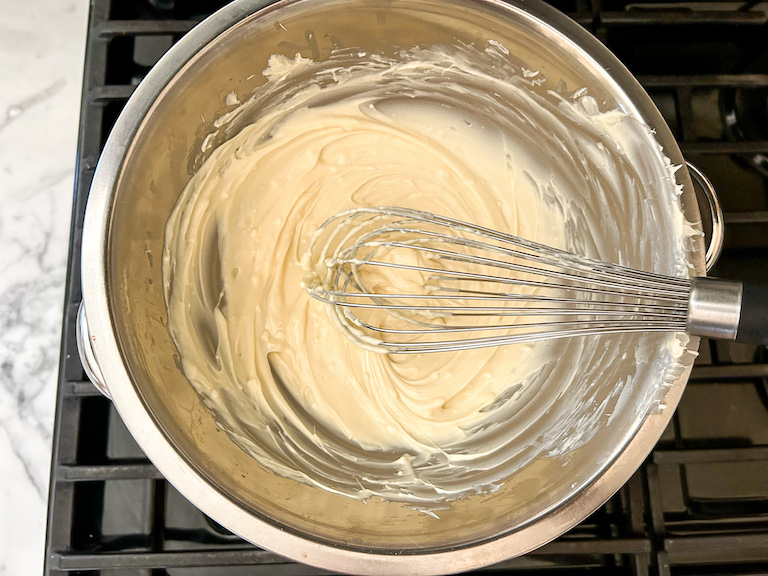 A bowl of melted white chocolate with a whisk
