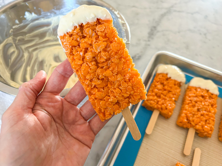 Hand holding a Krispie treat popsicle dipped in white chocolate