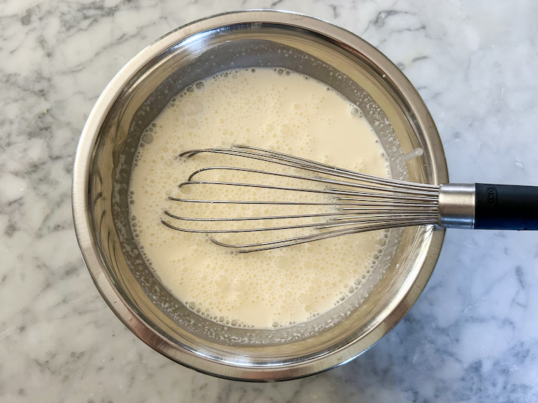 A bowl of milk and cream with a wire whisk