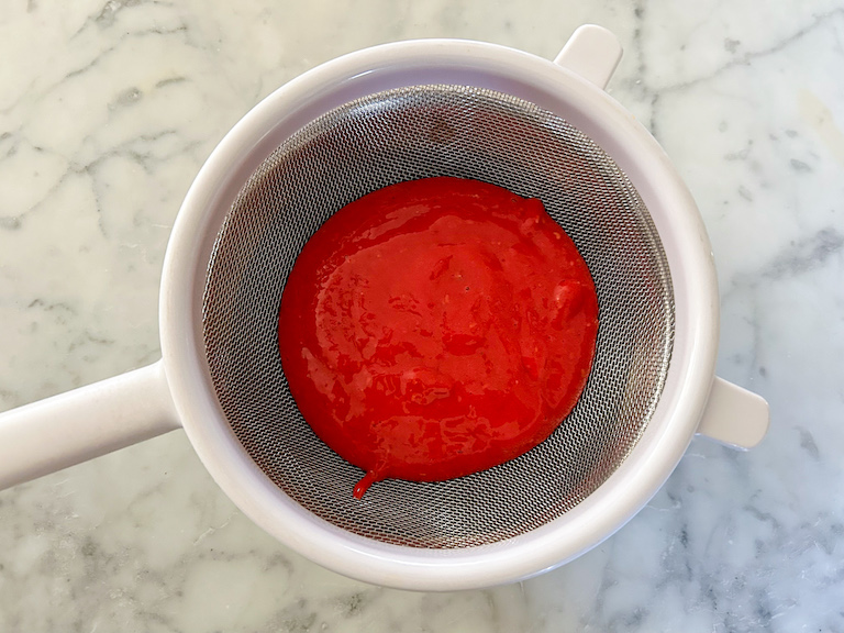 Passing raspberry puree through a mesh strainer