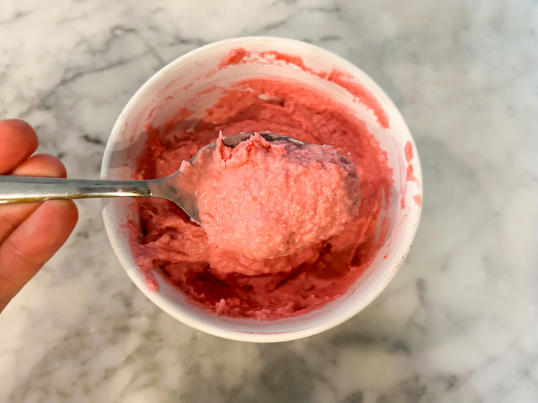 Hand holding a spoonful of raspberry sherbet