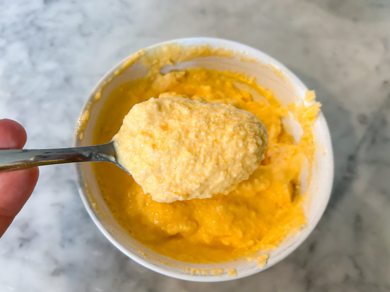 Hand holding a spoon with a scoop of orange sherbet