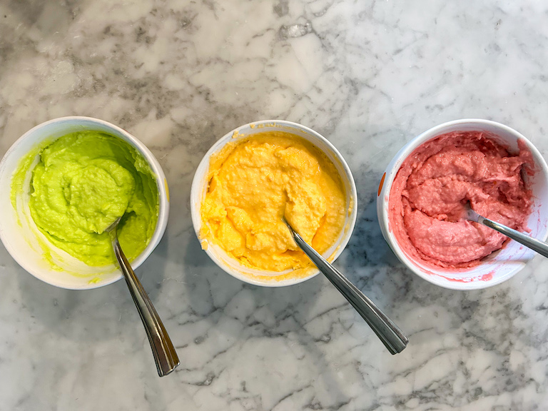 Small bowls of lime, orange, and raspberry sherbet on a marble surface