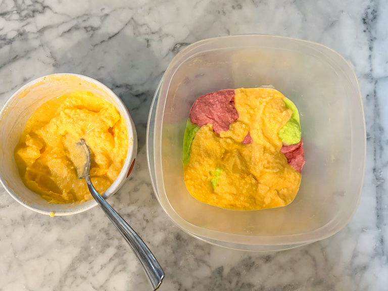 A bowl of orange sherbet and a plastic container on a marble surface
