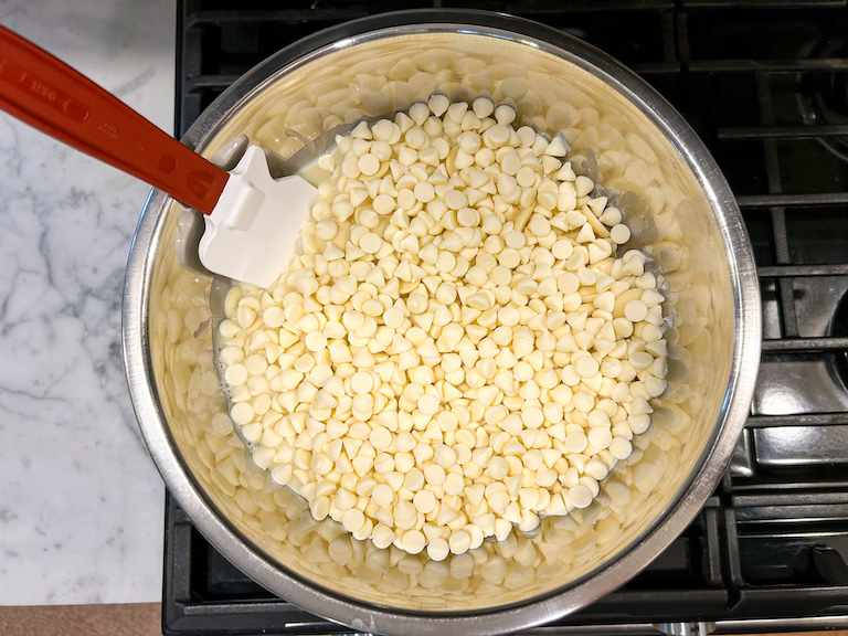 Sweetened condensed milk and white chocolate chips in a metal bowl on the stovetop