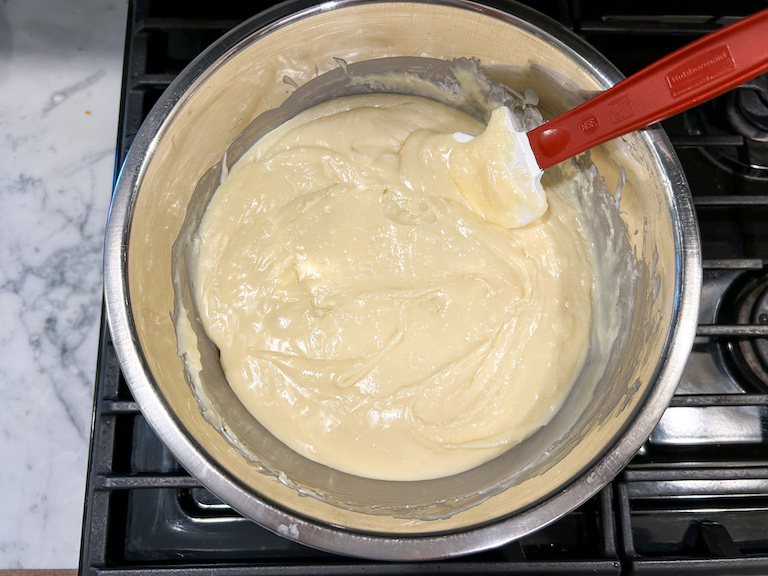A bowl of melted white chocolate on the stovetop with a spatula