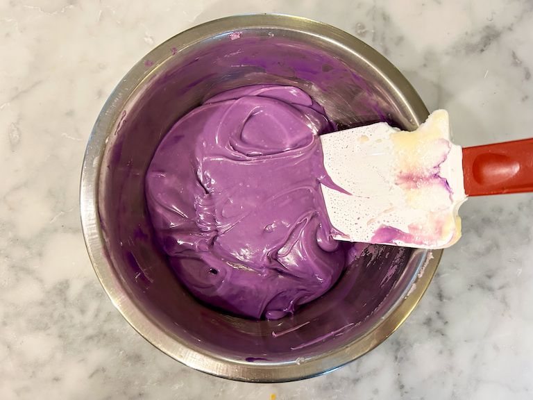 A bowl of melted purple chocolate with a rubber spatula