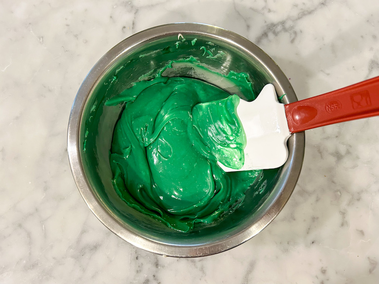 A bowl of melted green chocolate with a spatula