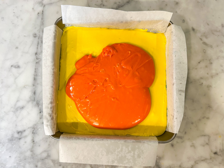 Melted orange chocolate layered over yellow fudge in a square tin