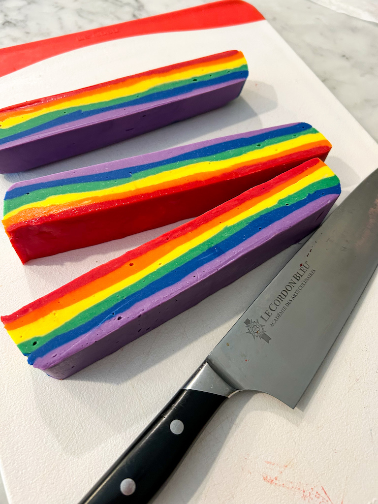Slices of rainbow fudge on a cutting board with a knife