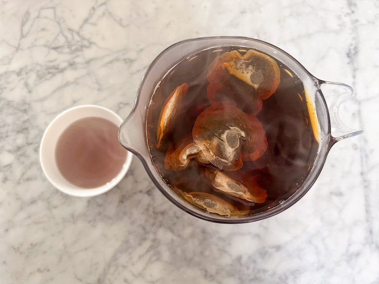 Black tea bags steeping in a pitcher, next to a dish of lavender syrup
