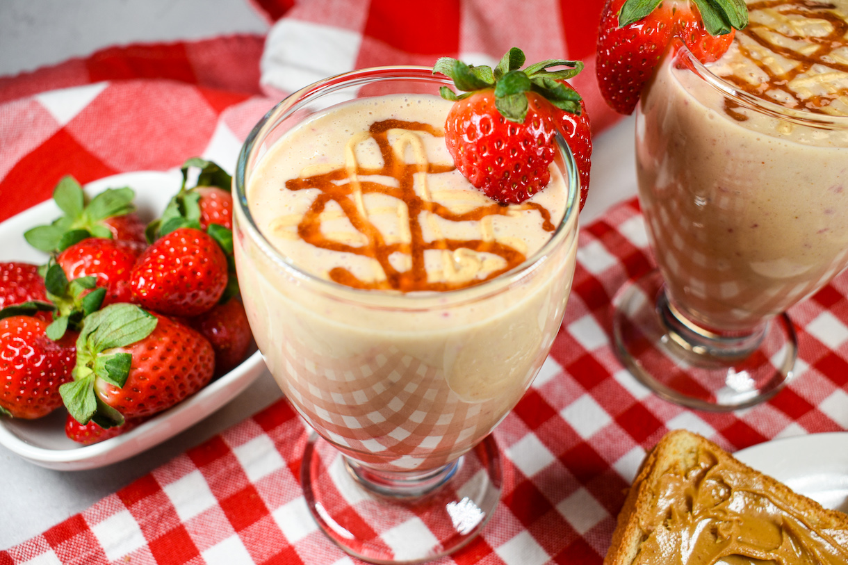 A PB&J smoothie garnished with a whole strawberry, positioned on a red checkered tea towel