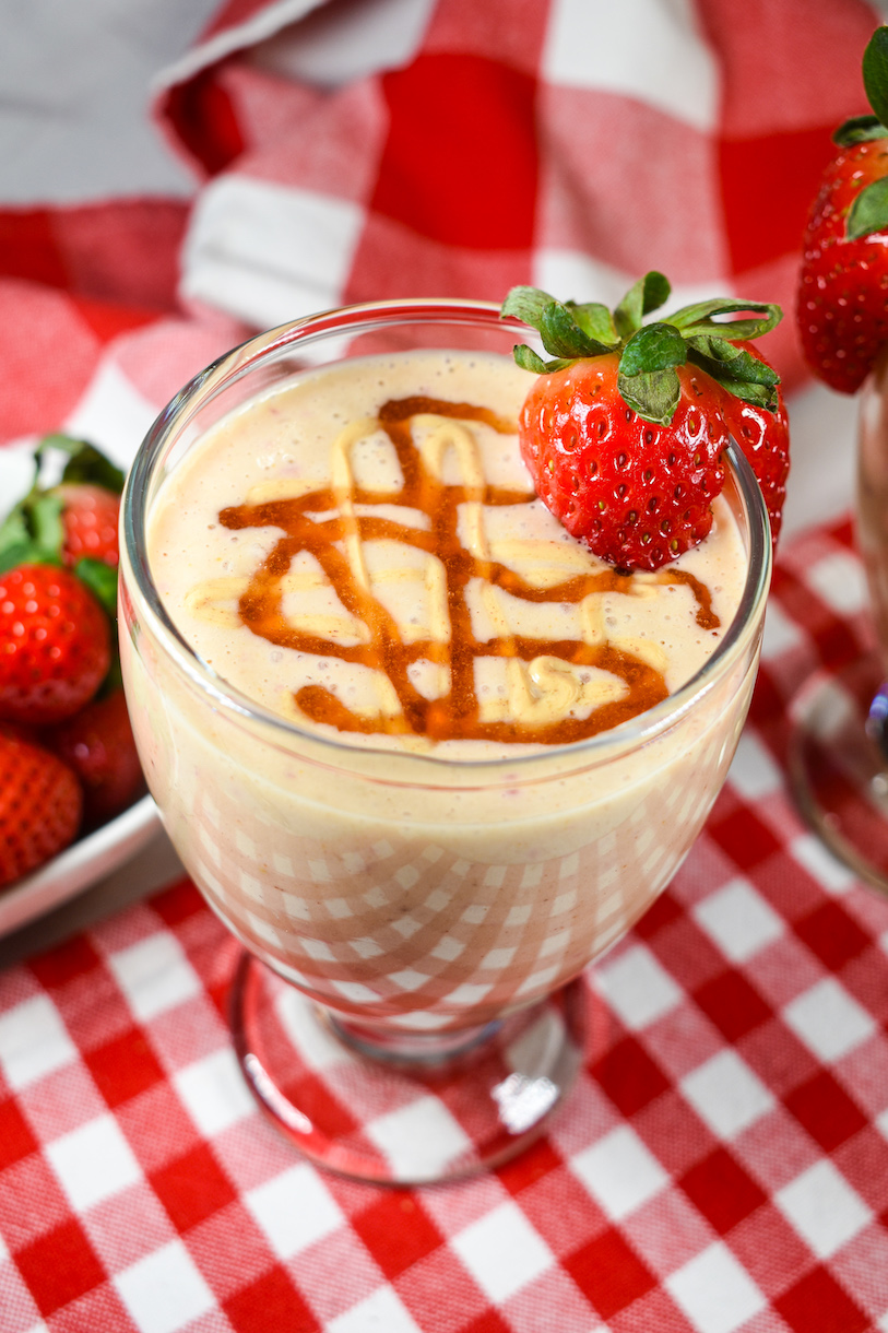 A peanut butter and jelly smoothie in a tall glass, arranged on a red checkered towel