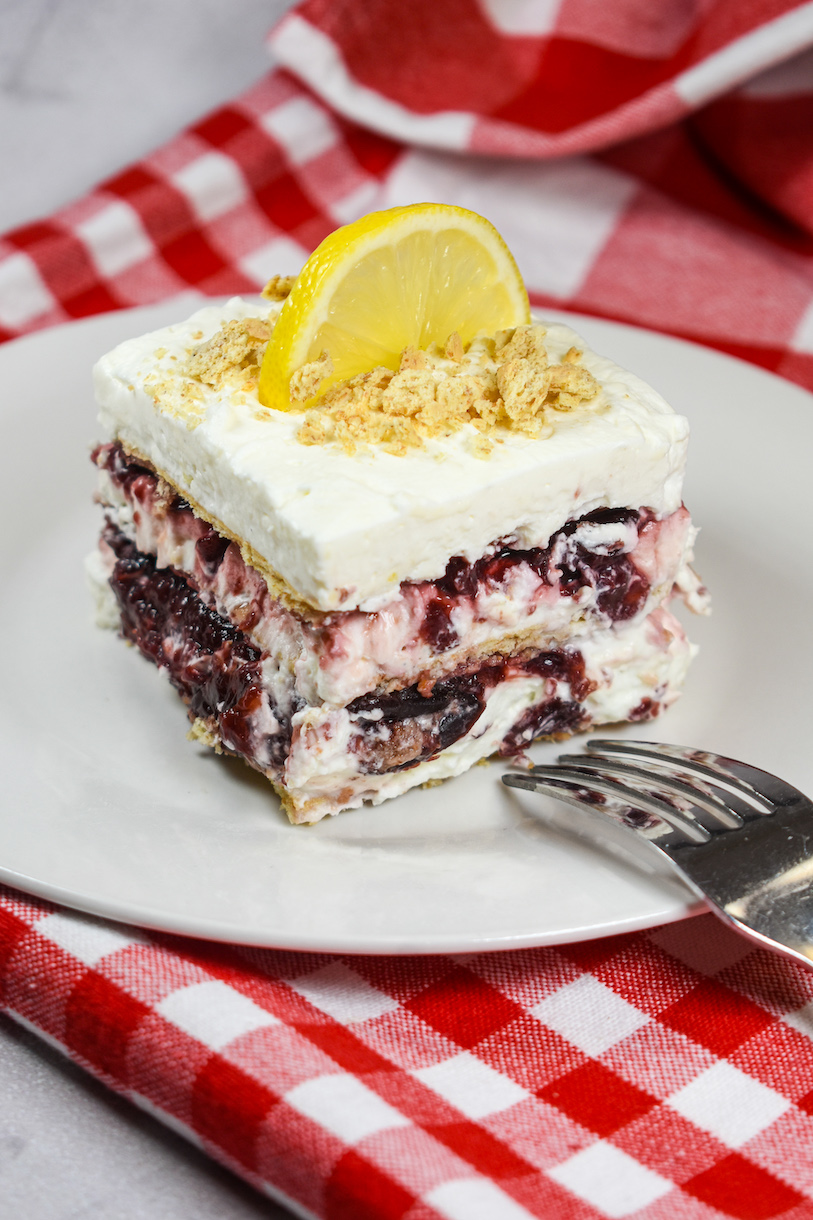 A slice of cherry cheesecake icebox cake garnished with graham cracker crumbs and a slice of lemon