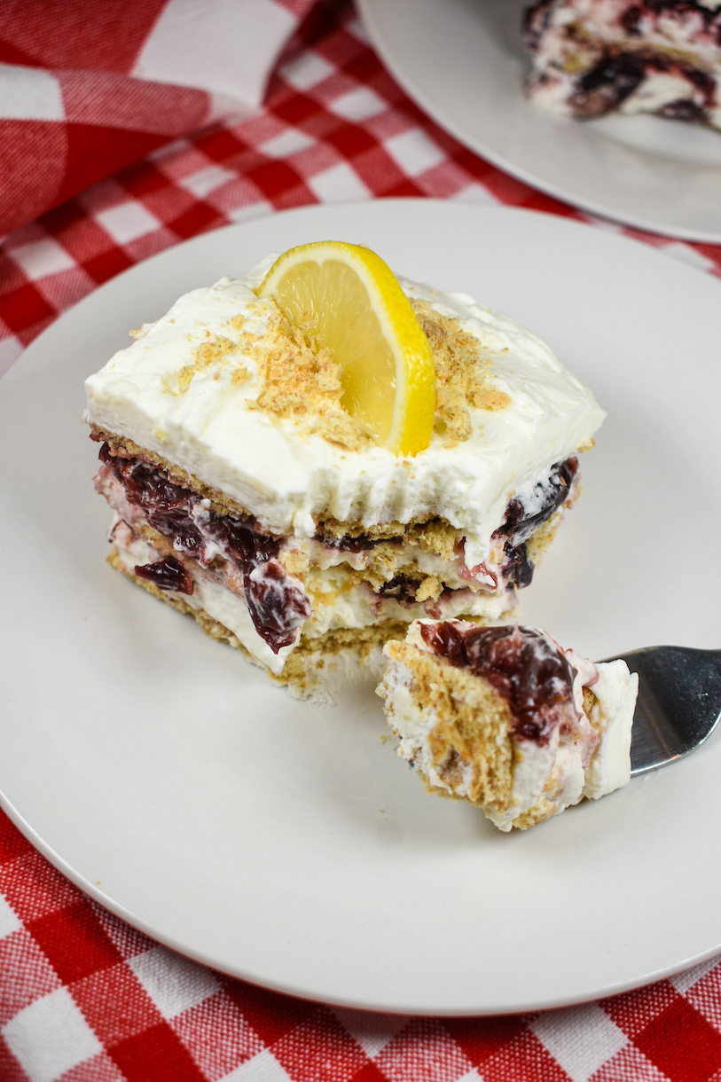 A slice of cherry cheesecake icebox cake on a plate, arranged on a red checkered tea towel