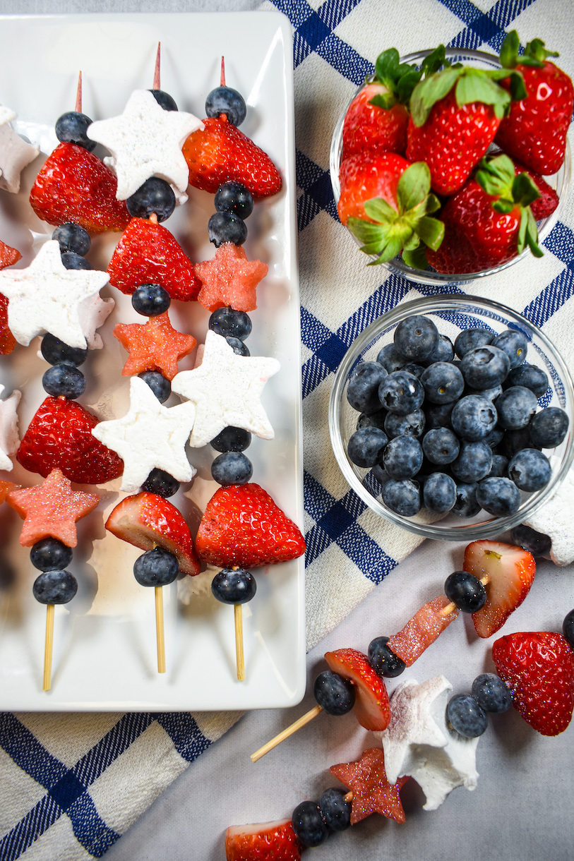 a plate of fruit skewers, dish of blueberries, and dish of strawberries