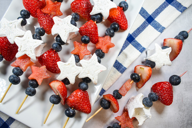 Strawberries, watermelon, blueberries, and star marshmallows threaded onto wooden skewers and arranged on a white plate