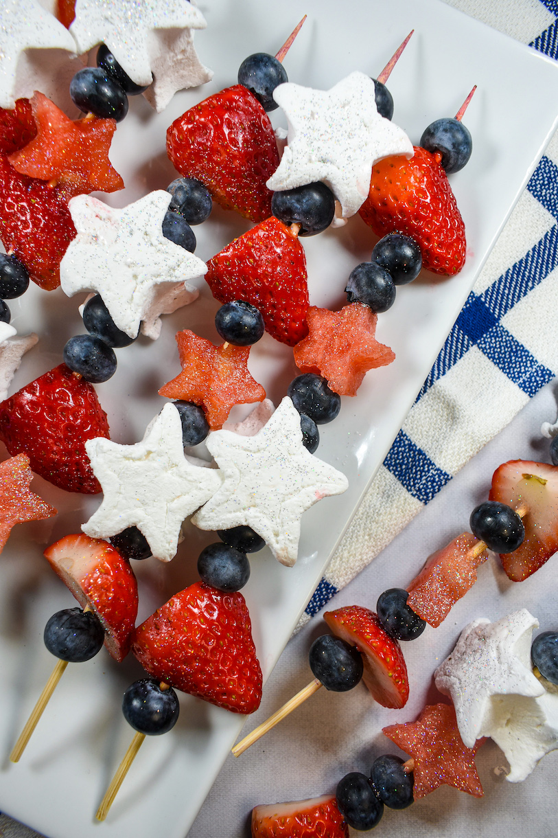 A platter of fruit skewers arranged on a plaid tea towel