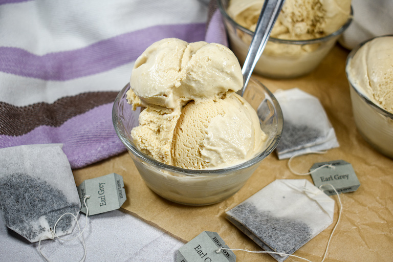 A dish of Earl Grey tea ice cream on a sheet of parchment with tea bags and a purple striped towel
