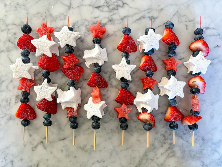 Fruit kebabs with marshmallows arranged on a marble surface