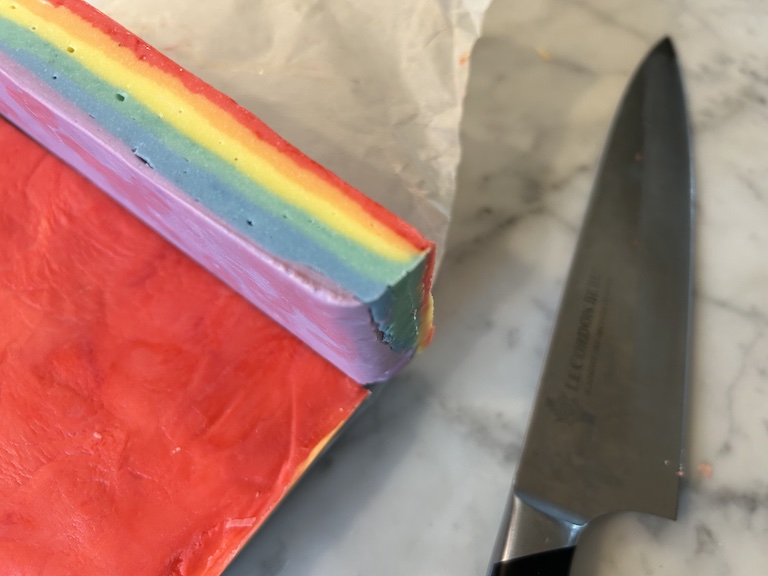 A slice of rainbow fudge on a marble surface with a knife
