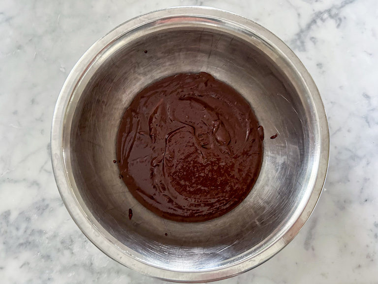 A bowl of chocolate ganache sitting on a marble surface