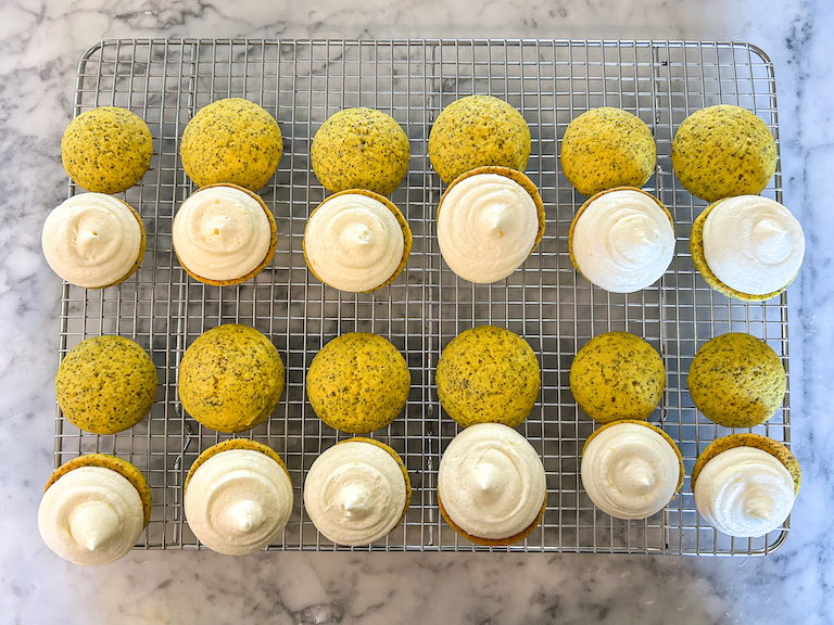 Lemon poppyseed whoopie pies on a wire rack, piped with lemon buttercream