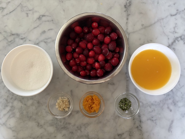 Ingredients for making cranberry compote, arranged in bowls on a marble surface