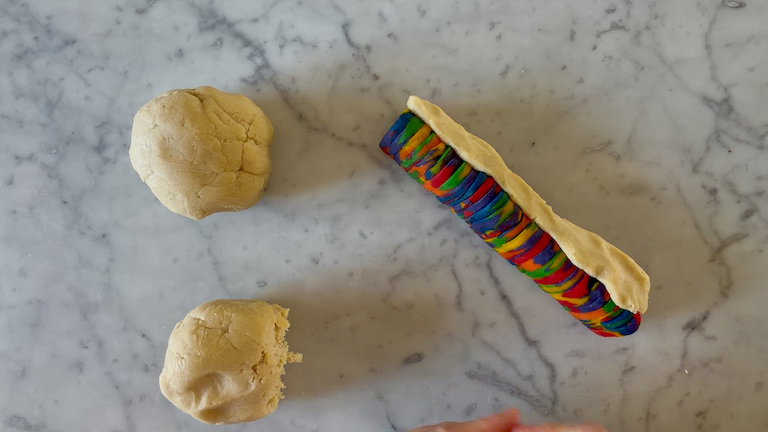 Two balls of cookie dough and a log of rainbow cookie dough on a marble surface