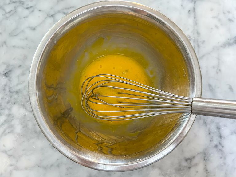 Egg yolks in a metal bowl with a whisk